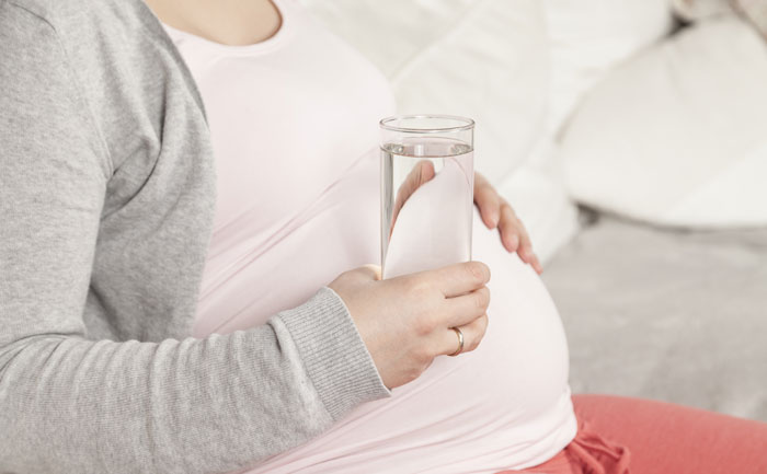 Une femme enceinte qui tient un verre d'eau dans sa main